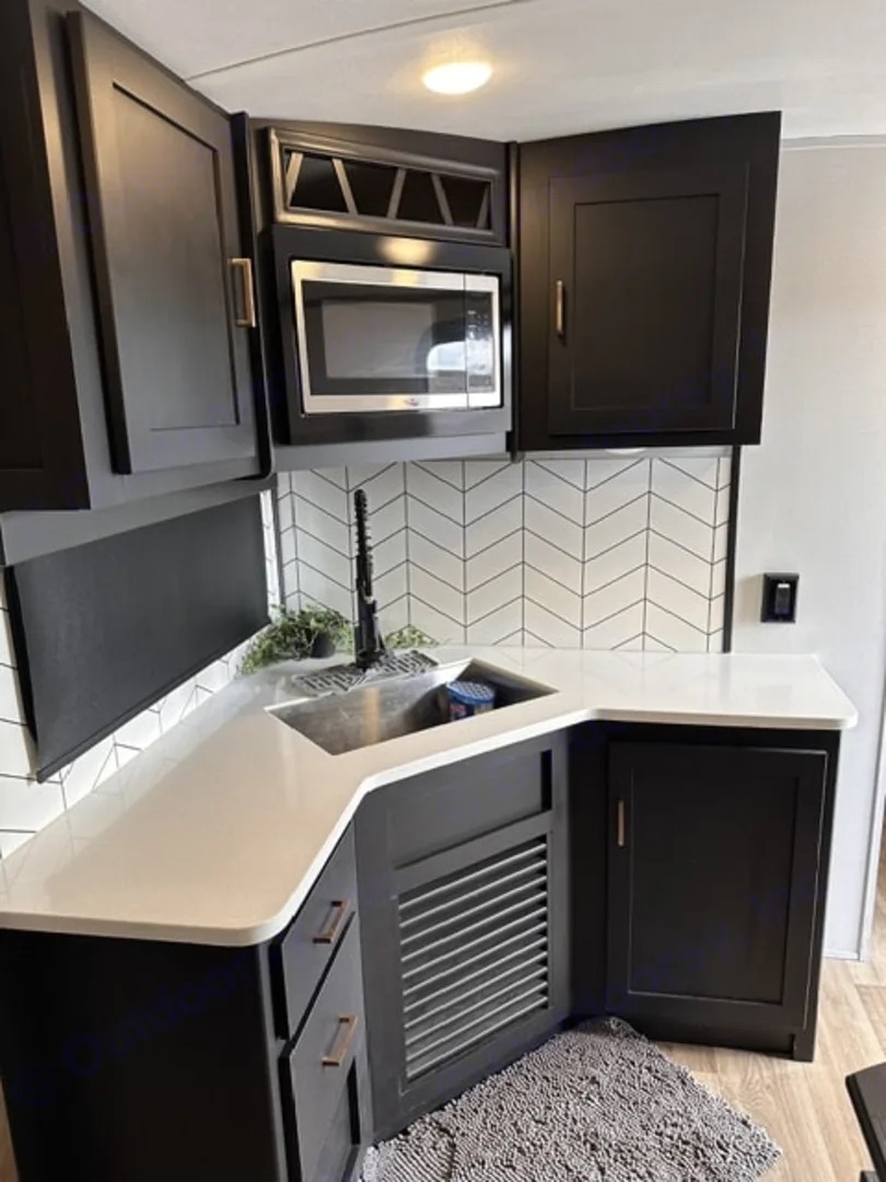 Camper kitchen with corner sink, counters, microwave and cabinets
