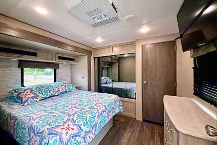 Camper main bedroom with queen bed, mirrored closet and television