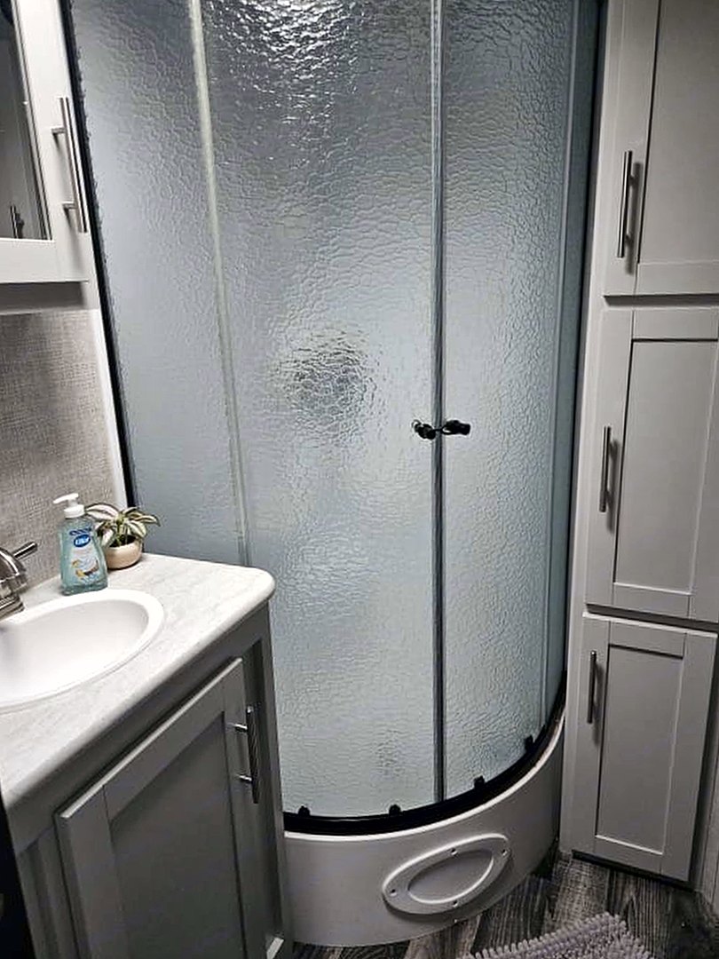 Camper bathroom with a vanity, corner shower, and linen cabinet