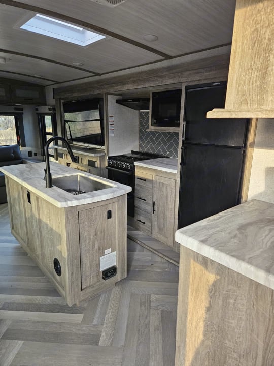 Camper kitchen island with a sink across from the range and refrigerator