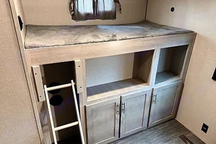 Camper bunk with storage cabinets, shelving and ladder