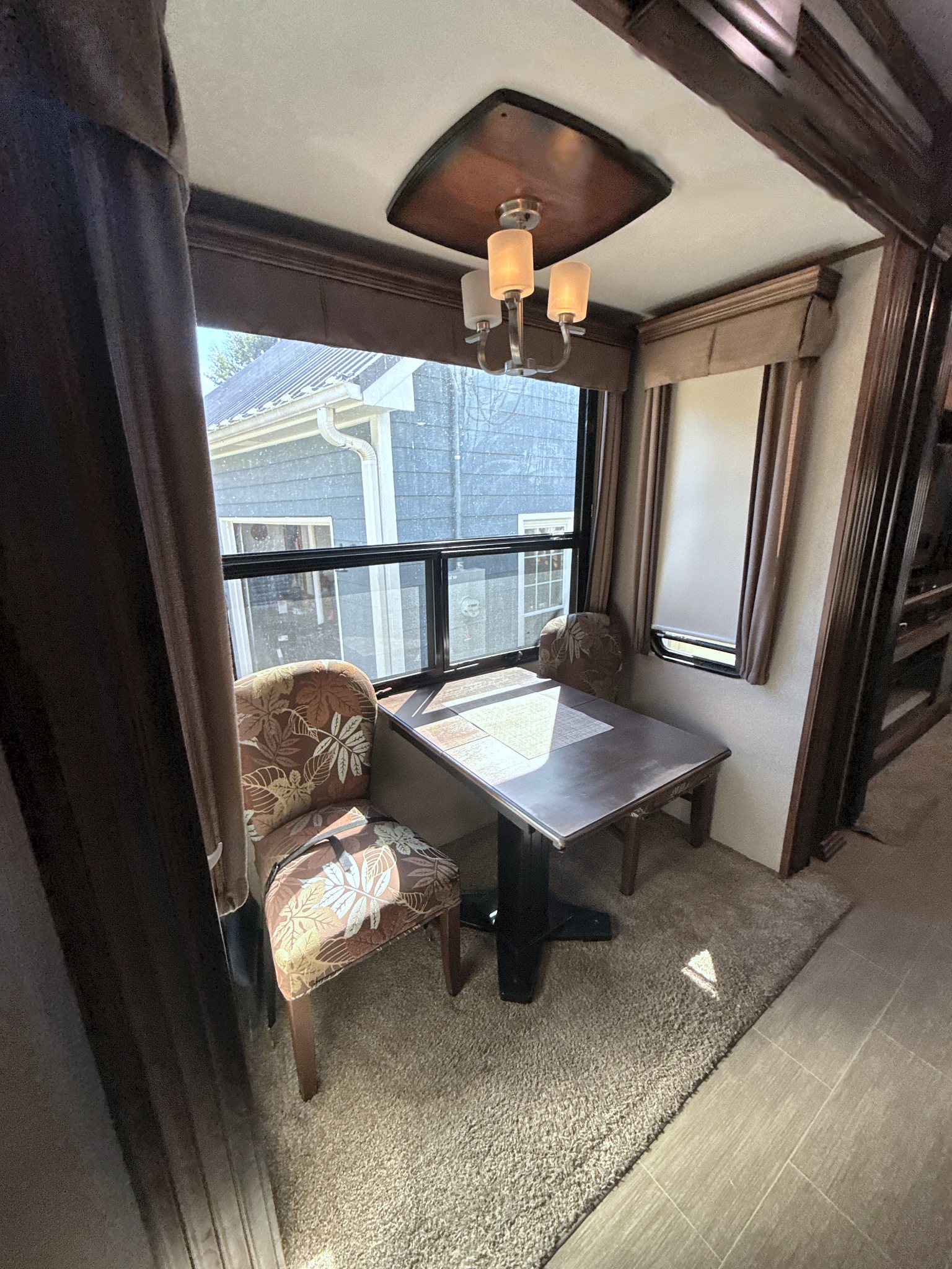 Camper dining table with two upholstered chairs beside a large window